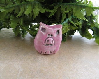 May include: A small pink ceramic pig figurine with a detailed face and snout.