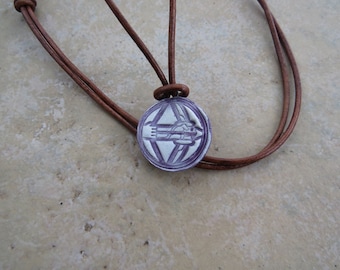 May include: A brown leather cord necklace with a round pendant featuring a white design of a spaceship inside a triangle.
