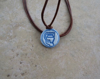 May include: A blue and white ceramic pendant with a water pitcher design hangs on a brown leather cord. The pendant is round and has a raised design.