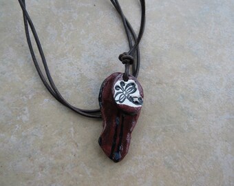 May include: A brown leather cord necklace with a red and black ceramic pendant featuring a white floral design.