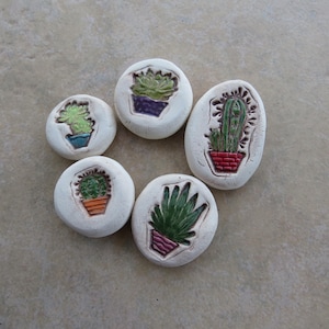 May include: Six white ceramic coasters with different green and brown cactus designs. Each coaster features a cactus in a pot.