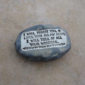 May include: A gray stone with a white inscription that reads "I will praise you, O Lord, with all my heart; I will tell of all your wonders. Psalm 9:1".