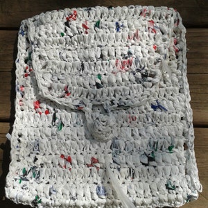 May include: White crocheted bag made from recycled plastic bags. The bag has a flap closure and a small, round handle.