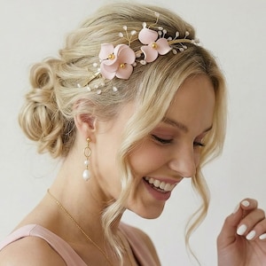 May include: A woman with blonde hair styled in an updo, wearing a pink dress and jewelry. She is wearing a floral headband with pink flowers and pearl accents. The jewelry includes a gold necklace with a pearl pendant and pearl earrings.
