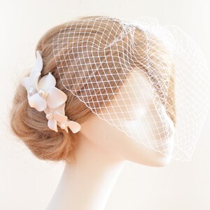 May include: A white bridal veil with a delicate floral hair comb. The comb features white flowers with pearl accents.
