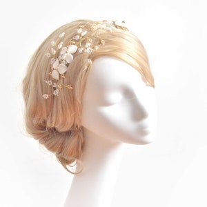 May include: A hair vine accessory featuring gold-toned wire branches adorned with small white flower petals, clear crystal beads, and tiny gold accents. The piece is arranged in a delicate, branching pattern designed to be worn along the side of the hair.