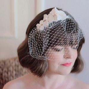 May include: A white bridal veil with a floral design. The veil is made of tulle and has a delicate floral pattern. The veil is worn by a person with short brown hair.