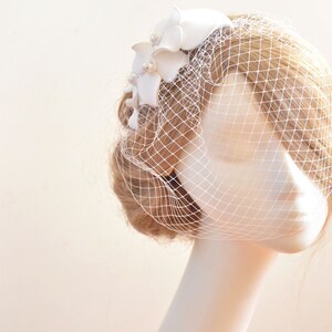 May include: White bridal veil with a white flower embellishment. The veil is made of a fine mesh material and is attached to a comb.