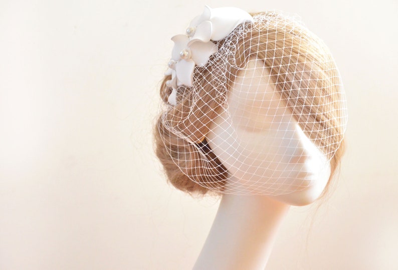 May include: White bridal veil with a white flower embellishment. The veil is made of a fine mesh material and is attached to a comb.
