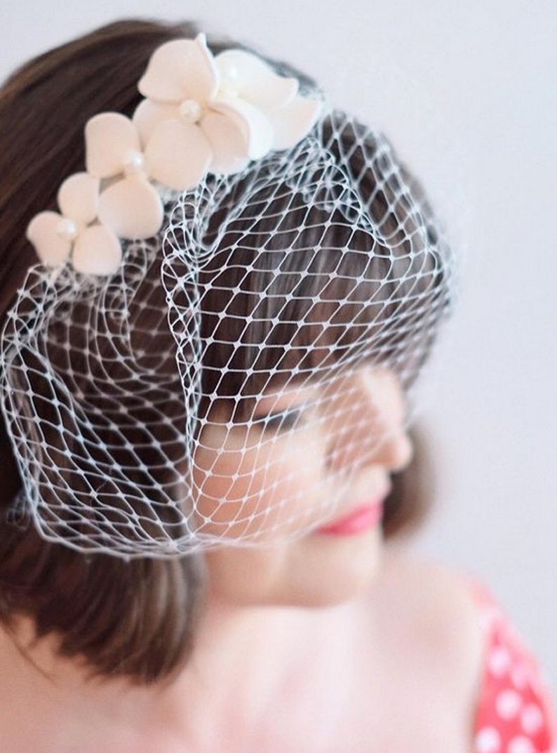 May include: A white bridal veil with a delicate floral design. The veil is made of soft tulle and features a row of white flowers.