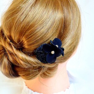 May include: A black fabric flower hair clip with a sparkly center. The clip is worn in a woman's blonde hair.
