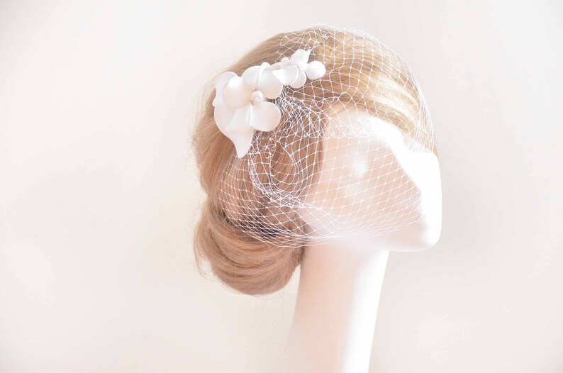 May include: White bridal veil with a white flower embellishment.