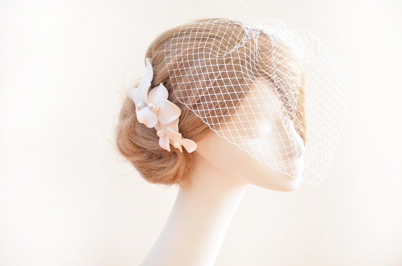 May include: A white bridal veil with a delicate floral hair comb. The comb features white flowers with pearl accents.