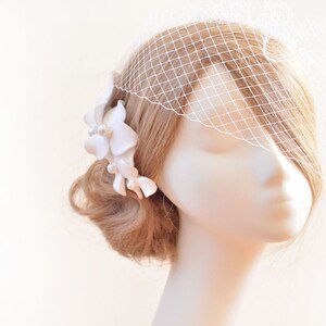 May include: A white bridal veil with a delicate floral hairpiece. The veil is made of a fine mesh fabric and is attached to a comb. The hairpiece features white flowers and pearls.