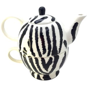 May include: A white ceramic teapot and teacup set, featuring a black zebra stripe design. The teapot has a lid with a black knob and a curved spout. The teacup is stacked beneath the teapot, with a matching handle.