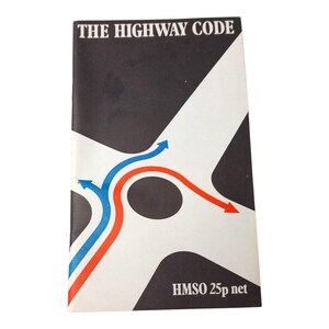 May include: A vintage copy of "The Highway Code" booklet. The cover features a black and white abstract design with blue and red curved lines and arrows. The text "THE HIGHWAY CODE" is at the top.