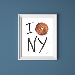 May include: A white framed print with black text that reads "I  NY" with a bagel in the center of the "O".