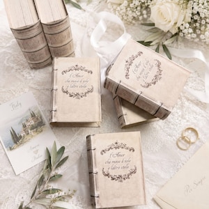 Op de afbeelding: Meerdere rechthoekige doosjes ontworpen als vintage boeken met beige covers en donkerbruine ruggen. Elk doosje heeft een sierlijk kader rondom de Italiaanse tekst, L'Amor che move il sole e l'altre stelle, gedrukt in een donkerbruin lettertype.