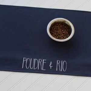 May include: Navy blue pet food mat with white text that reads "POUDRE & RIO".