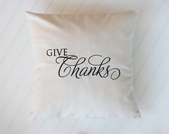 May include: A white throw pillow with the text "GIVE THANKS" in black cursive lettering.