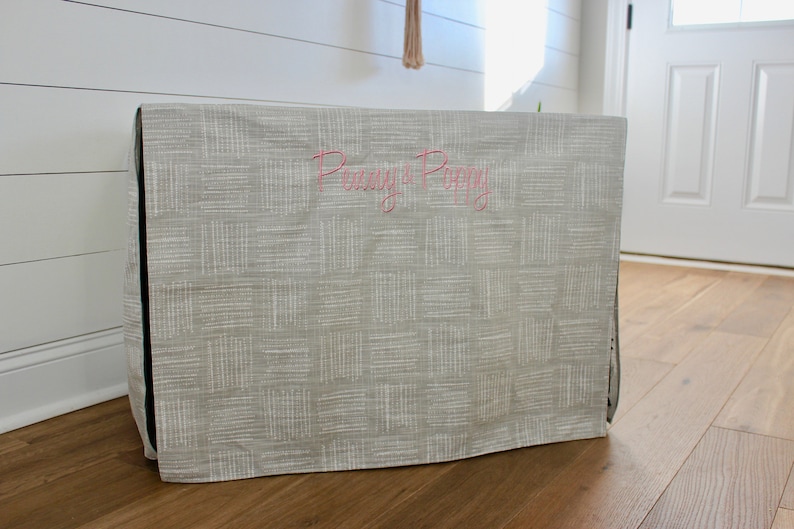 May include: A gray and white patterned dog crate cover with the text "Penny & Poppy" embroidered in pink.
