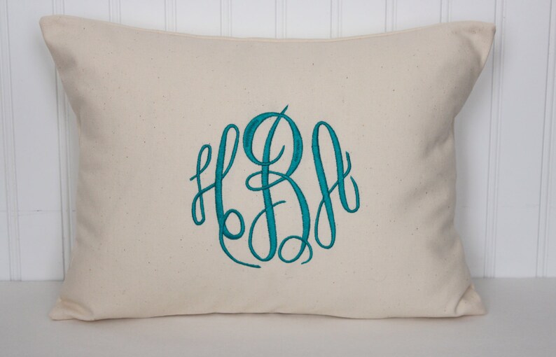 Puede incluir: Una almohada blanca con un monograma azul turquesa de las letras "LBA" bordado en una fuente de escritura.