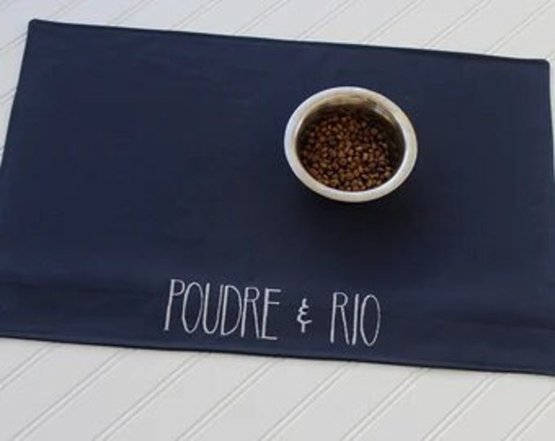 May include: Navy blue pet food mat with white text that reads "POUDRE & RIO".