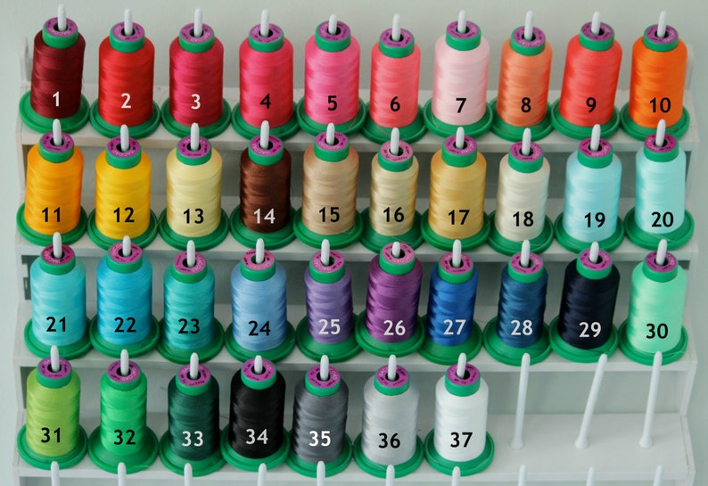May include: A set of 37 spools of thread, arranged in rows on a white shelf. The spools are numbered 1 to 37. The thread colours include red, yellow, blue, green, purple, black, white, and beige.