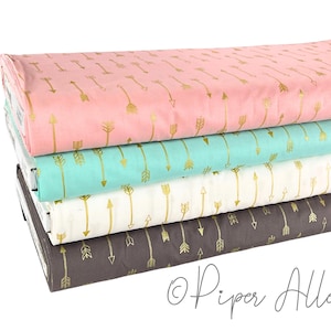 May include: A stack of four fabric rolls in pastel colors: pink, teal, white, and gray. Each fabric features a repeating pattern of gold arrows. The fabric is likely for sewing or crafting projects.