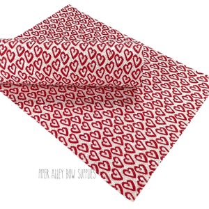 May include: White faux leather with a red glitter heart pattern.  The fabric is perfect for crafting projects like hair bows, headbands, and other accessories.  "PIPER ALLEY BOW SUPPLIES" is printed in the bottom right corner.