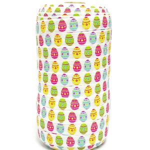 May include: A roll of white ribbon decorated with colorful Easter egg patterns. The eggs are in various colors, including pink, yellow, green, and blue, with floral and dotted designs. The ribbon is tightly wound, showcasing the repeating pattern.