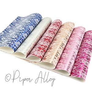 May include: Six sheets of faux leather with a white lace pattern on a metallic background. The sheets are arranged in a fan shape, with the colors ranging from blue to pink.