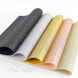 May include: A collection of glitter sheets in various colors, including black, silver, gold, rose gold, and light gold. The sheets are arranged in a fan shape, showcasing their sparkling texture. The image is well-lit, highlighting the shimmer of the glitter.