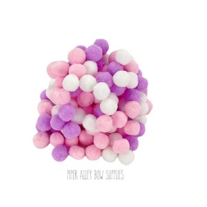 May include: A pile of white, pink, and purple pom poms. The pom poms are soft and fluffy and would be great for crafting.