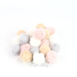 May include: A pile of fluffy pom poms in various shades of pink, gray, and beige. The pom poms are arranged in a loose pile, with some overlapping.