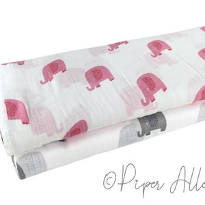 May include: Two rolled baby blankets. The top blanket is white with pink elephants. The bottom blanket is white with gray elephants. The blankets are made of a soft, lightweight fabric.