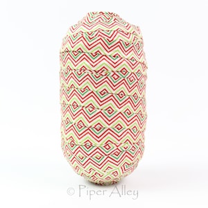 May include: A fabric-covered, cylindrical object with a festive pattern of red and green zigzags on a cream background. The object has a rounded top and bottom, and the fabric appears to be wrapped around it in layers. The overall shape is reminiscent of a decorative item.