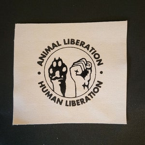 May include: A white patch with a black circle containing a paw print and a fist, with the text "ANIMAL LIBERATION" above and "HUMAN LIBERATION" below.