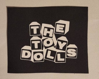 Puede incluir: Parche de tela negro con letras blancas que dicen "THE TOY DOLLS" en una fuente de bloque.