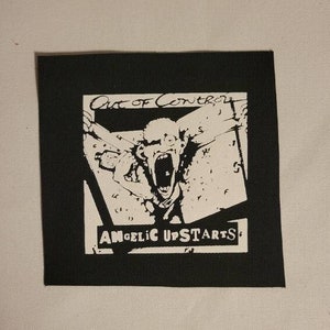 以下が含まれることがあります： 叫び声を上げている顔と「Out of Control」と「Angelic Upstarts」の文字が書かれた白黒のパッチ。