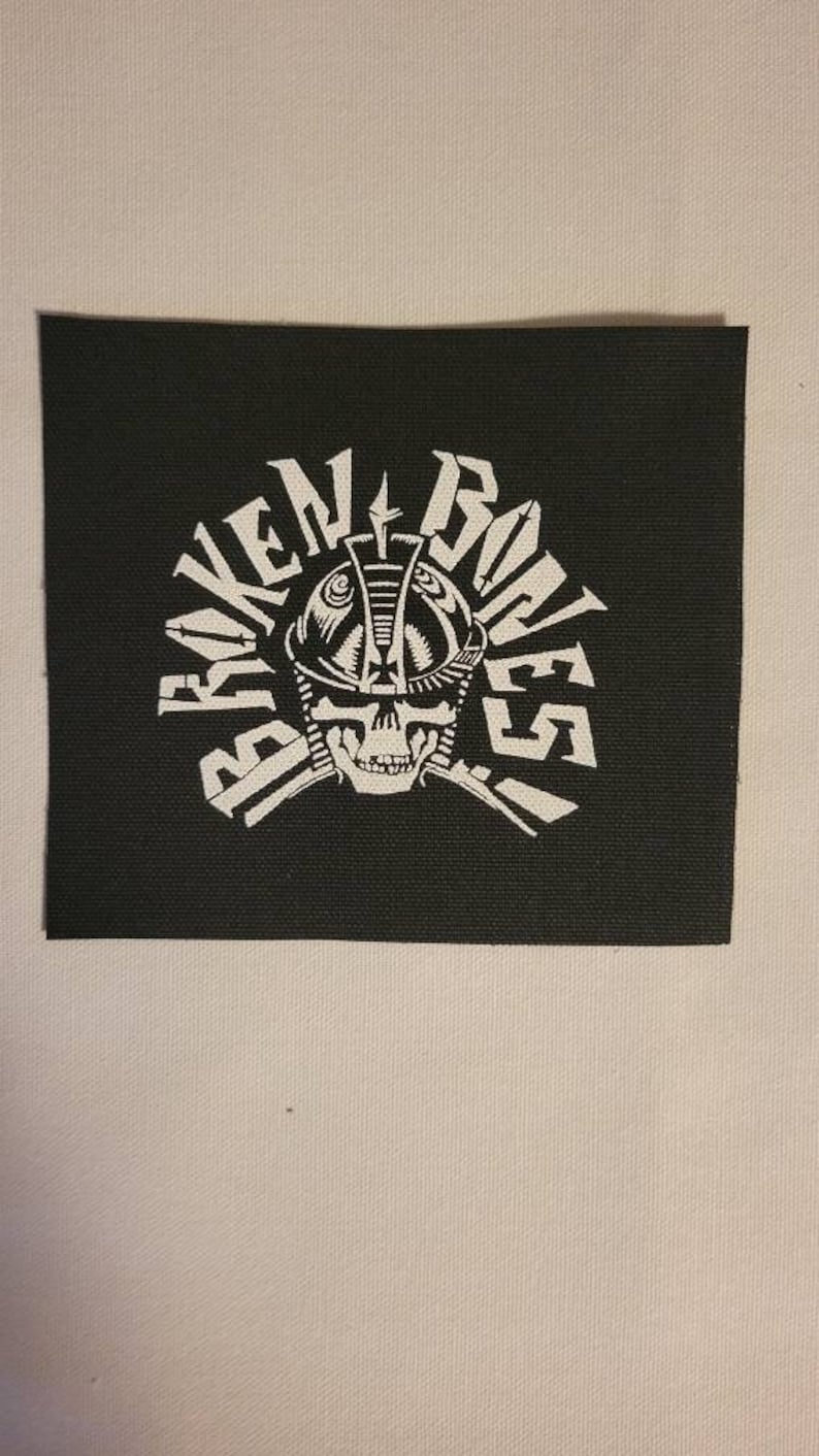 May include: Black and white embroidered patch with the text "Broken Bones" in a circular design. A skull wearing a helmet is in the centre of the patch.
