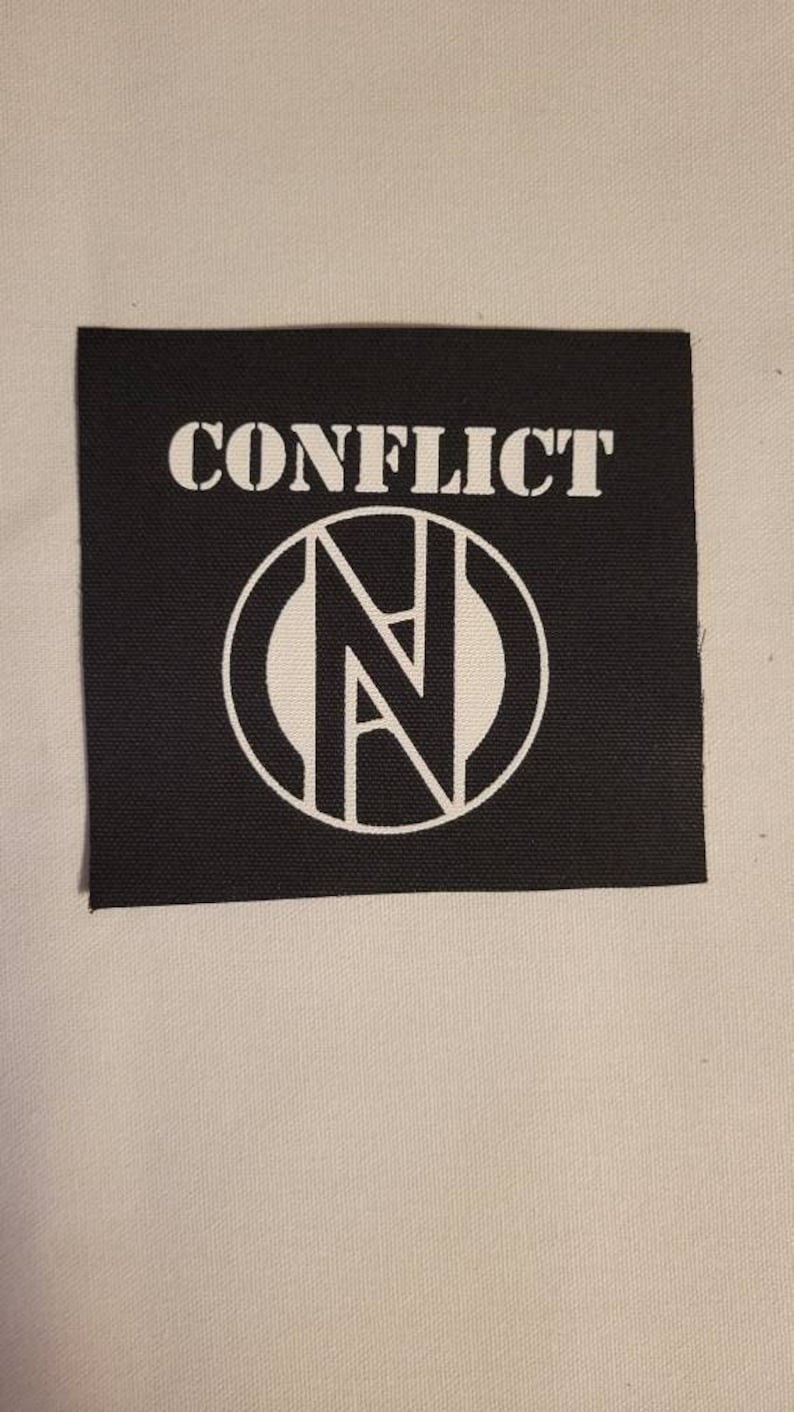 May include: Black and white embroidered patch with the word "CONFLICT" and a stylized "N" inside a circle.