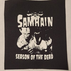 Op de afbeelding: Zwart-witte patch met de bandnaam "SAMHAIN" en de tekst "SEASON OF THE DEAD" in een vet, wit lettertype.
