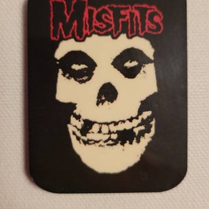 May include: A black and white sticker with a red "Misfits" logo and a white skull with black eyes and mouth.