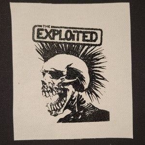 Pode incluir: Patch preto e branco com uma caveira com um mohawk e o texto "THE EXPLOITED" em um retângulo.