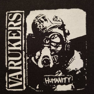 May include: Black and white patch with a person wearing a gas mask and a helmet. The text "WARUKERS" is on the left side of the patch and the text "HUMANITY" is on the bottom right side of the patch.