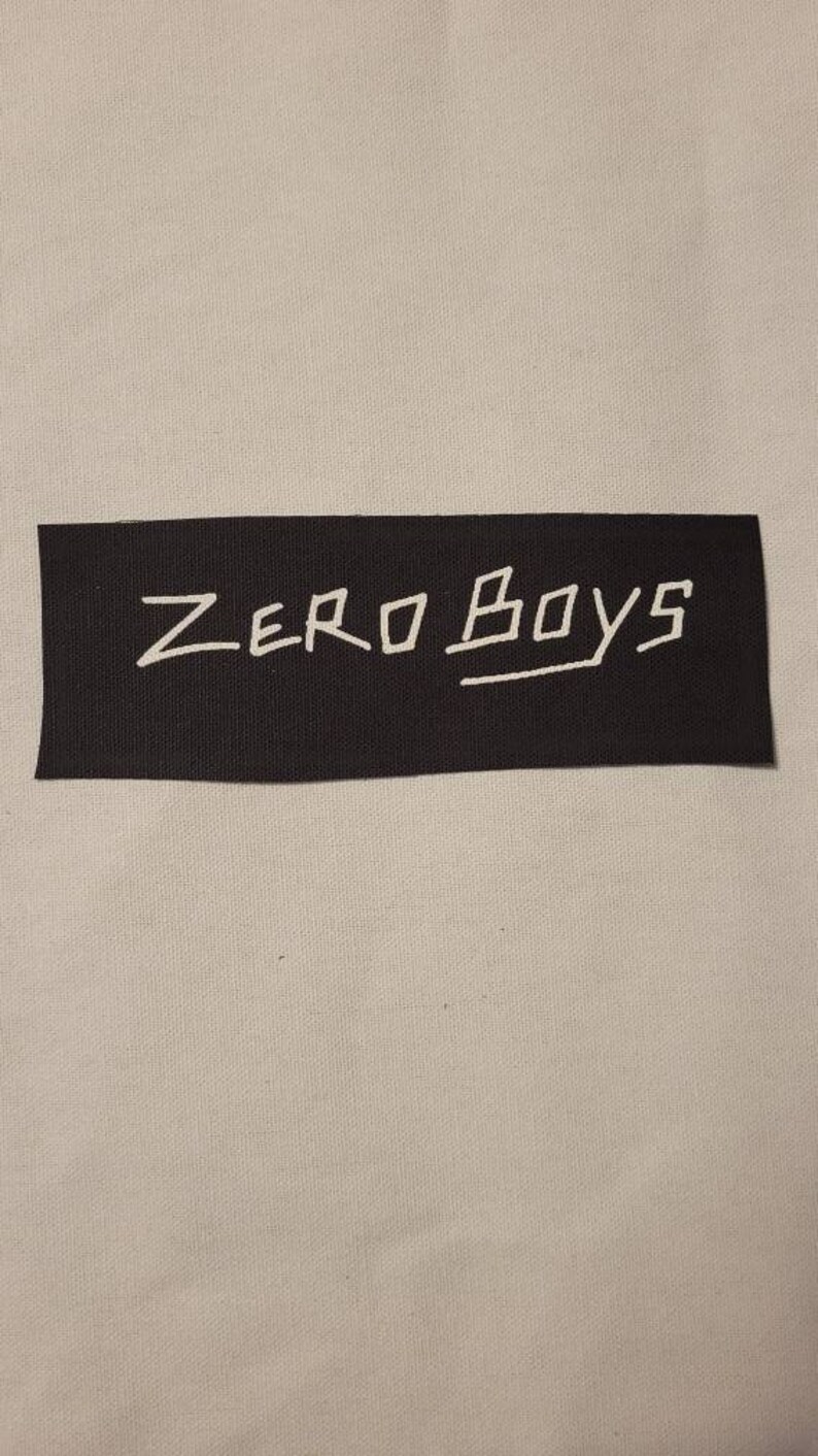 K&ouml;nnte beinhalten: Schwarzer Stoff-Patch mit wei&szlig;em Text, der "ZERO BOYS" lautet.