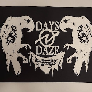 Pode incluir: Patch preto e branco com o texto "DAYS OF DAZE" em um círculo com uma seta. Duas figuras de pássaros esqueléticos flanqueiam o texto.