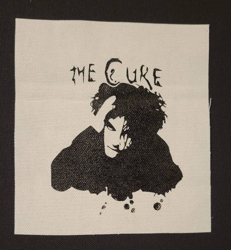 Puede incluir: Un parche de tela blanco con tinta negra que representa una silueta de una persona con el texto "THE CURE" sobre la persona.