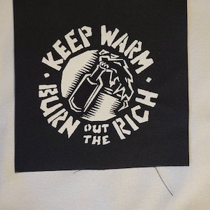 May include: Black and white patch with a circle design. The circle contains a hand holding a Molotov cocktail. The text around the circle reads "Keep Warm. Burn The Rich."